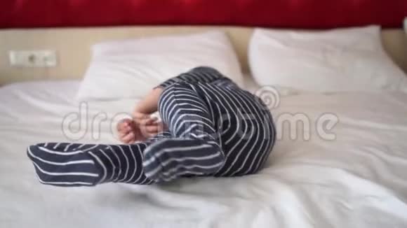 一个穿着条纹连衣裙的小男孩正在旅馆的一张大床上旋转动作缓慢视频的预览图