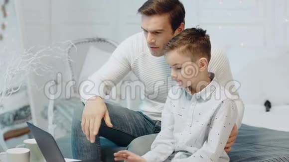 微笑的父子在豪华住宅的笔记本电脑上聊天视频的预览图