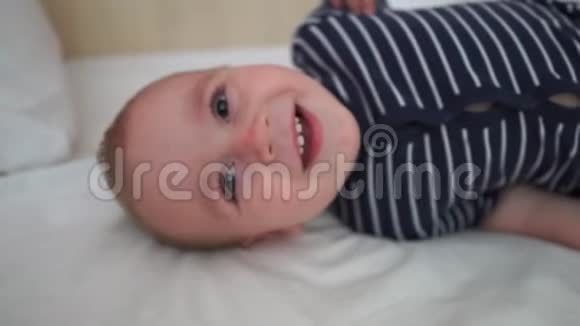 微笑的婴儿慢慢地躺在白色床单上的大床上视频的预览图