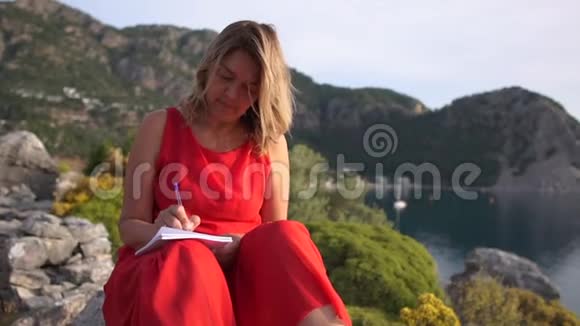 一个女人坐在海面上的岩石上缓慢地做笔记视频的预览图