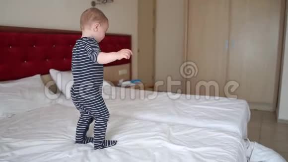 一个可爱的男孩玩得很开心摔倒在旅馆房间的大床上动作很慢视频的预览图