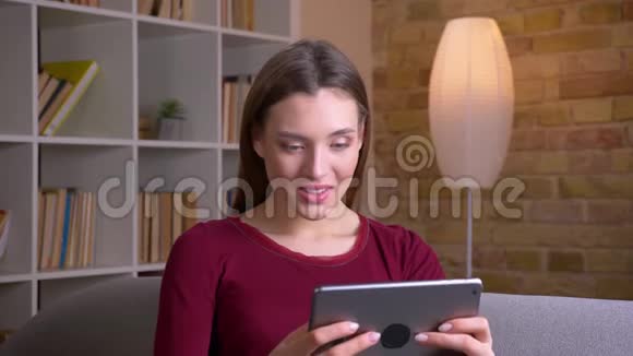 年轻漂亮的黑发女人在平板电脑上玩游戏非常快乐地转向相机和微笑在家里视频的预览图