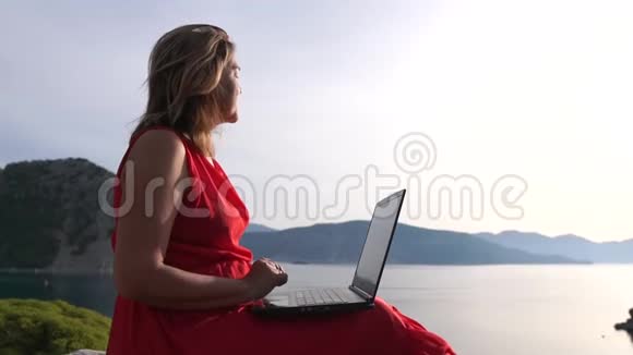 微笑的女人坐在漂亮的海景旁用笔记本电脑打字动作很慢视频的预览图