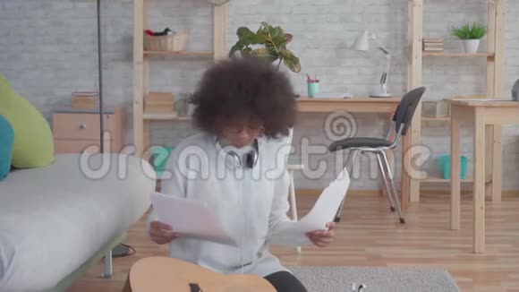 有非洲发型的开朗的非裔美国女人弹吉他坐在地板上慢悠悠视频的预览图