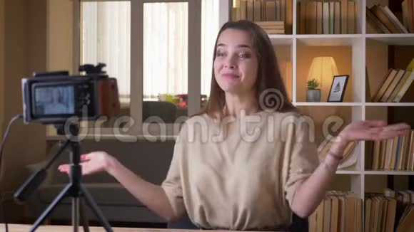 年轻有魅力的白种人女性博客写手在镜头前讲话在室内展示大拇指视频的预览图