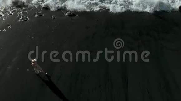 西班牙加那利群岛的特内里费一个女孩漫步在黑色火山海滩的俯视图视频的预览图