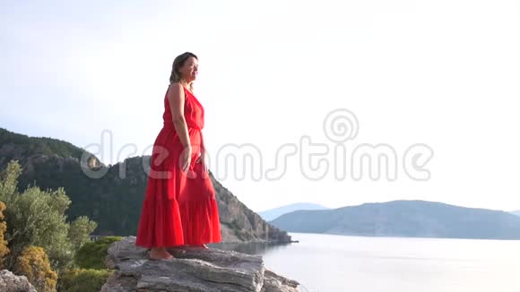 漂亮的成年女人站在高高的海面上的岩石上做个手势一切都好视频的预览图