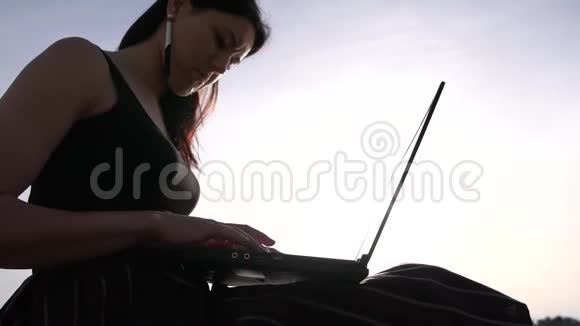 一个黑发女人在一台笔记本电脑上工作光着脚坐在海面上的岩石上视频的预览图