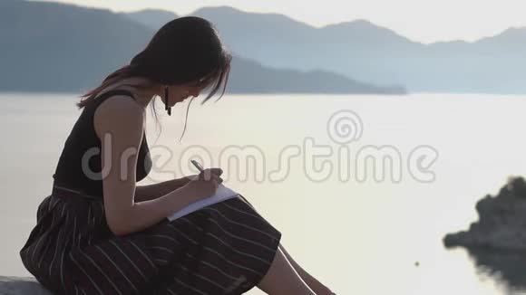 小女孩在笔记本上写字慢悠悠地坐在海滨视频的预览图