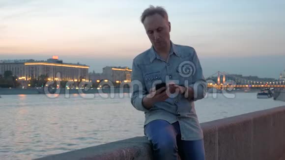 黄昏时分中年人在河堤上使用手机视频的预览图