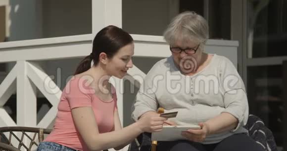 女儿在阳光明媚的日子里用信用卡在户外微笑帮助年迈的母亲上网购物视频的预览图