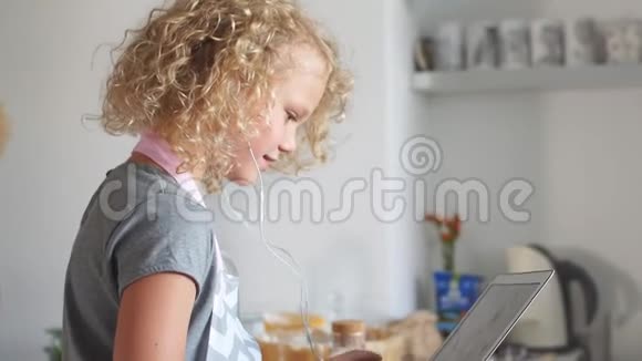 可爱的白种人女孩坐在桌子旁用笔记本电脑用耳机听声音视频的预览图