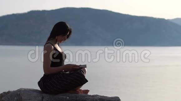 浪漫的女孩在日出时热情地在海边读一本书慢动作视频的预览图