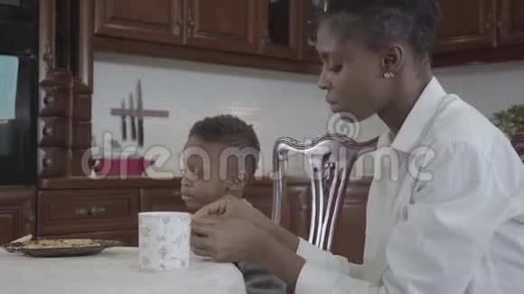 一位非裔美国妇女和她的小儿子坐在桌旁在盘子上玩饼干母子关系视频的预览图
