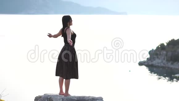 美丽的女孩祈祷感谢上帝站在海边的岩石上慢动作视频的预览图
