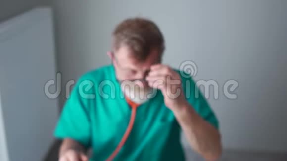 一位年长的医生身穿绿色医用长袍的教授填写了一份病人病历看着摄像机视频的预览图
