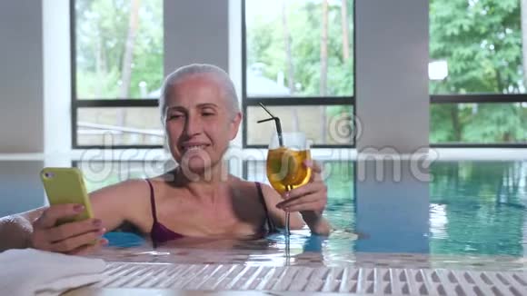 在泳池里带着电话和鸡尾酒的老太太视频的预览图