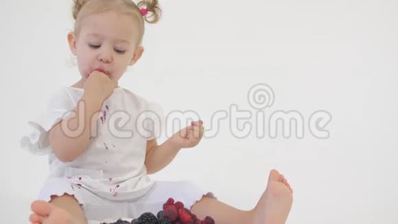 穿白色衣服的小女孩吃浅色背景的多汁浆果视频的预览图