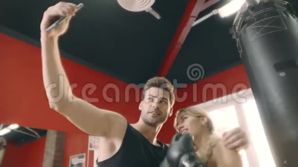 在健身馆里一对快乐的情侣拥抱在一起拍手机自拍视频的预览图
