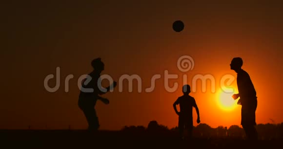 三个男孩在日落时踢足球日落时孩子们玩球的剪影幸福家庭的概念视频的预览图