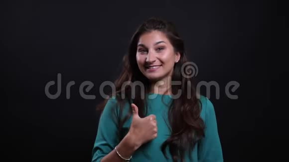 年轻漂亮的黑发女性的特写镜头拇指向上开心地微笑着看着背景的镜头视频的预览图