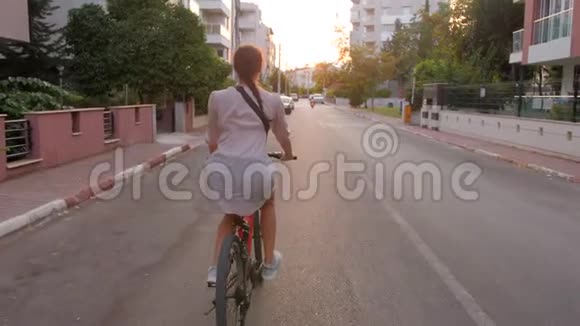 美丽的夏日心情拍摄的年轻女子骑着自行车在时尚的户外踩着夕阳的光芒视频的预览图