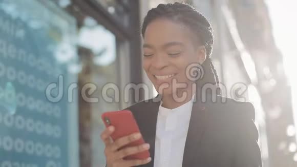 快乐的非洲女商人使用智能手机站在商业中心附近的街道上黑色时尚可怕的家伙女性视频的预览图