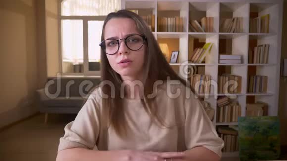 年轻有魅力的高加索女性博客写手戴着眼镜在室内直播着镜头视频的预览图