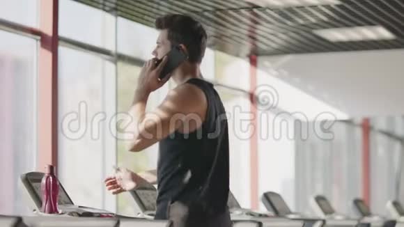 健身俱乐部里的运动员在跑步机上用手机说话视频的预览图