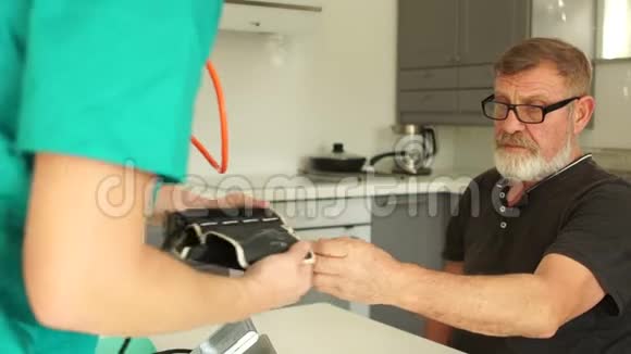 年轻的医生或护士测量一个老人在他的家里在厨房的血压紧急救护视频的预览图