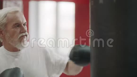 灰发男子训练踢到拳击袋在搏击俱乐部积极的高级概念视频的预览图