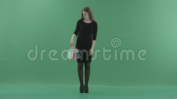 漂亮的笑女人穿着黑色的小裙子在摆姿势和玩购物袋她站在视频的预览图