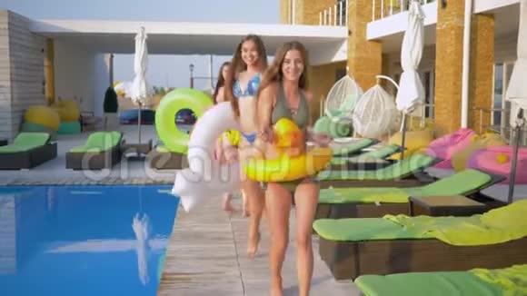 夏日度假期间快乐迷人的女朋友们穿着带充气环的泳衣在游泳池附近散步视频的预览图