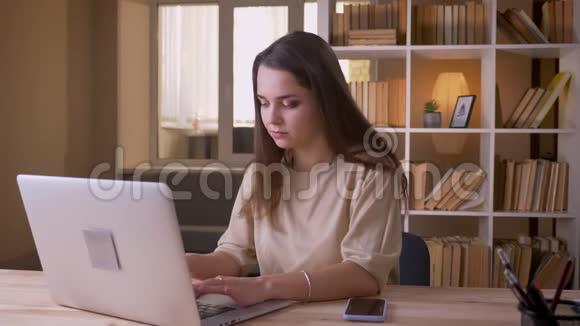 一位年轻迷人的高加索女商人的特写肖像她用笔记本电脑把手机放在室内的桌子上视频的预览图