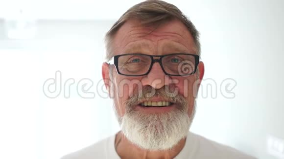快乐善良的祖父留着灰色胡子微笑着大师在镜头前一个年长的男人白色的肖像视频的预览图