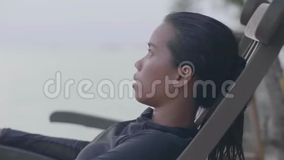 一个年轻无忧无虑的女人坐在海滩上的椅子上的肖像视频的预览图