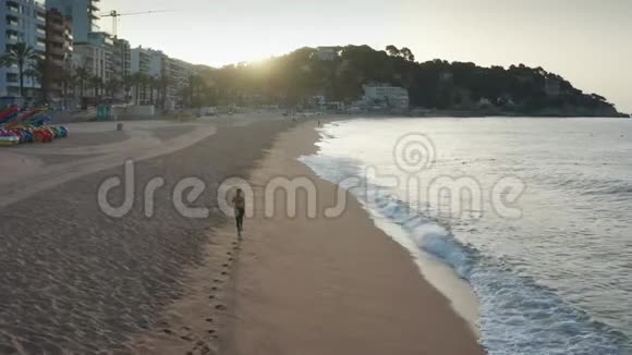 日出时在海滩慢跑的女性的鸟瞰图视频的预览图