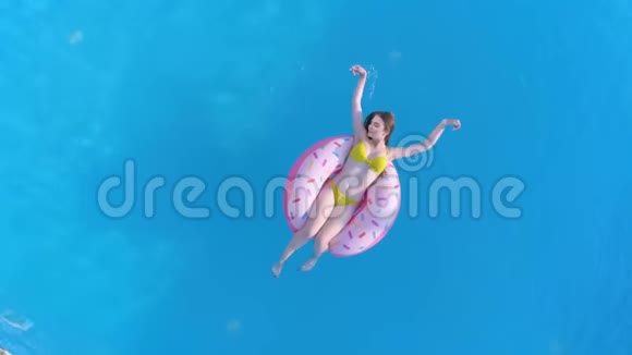 夏天休息快乐的女孩穿上泳衣在游泳池边的充气环在昂贵的度假胜地休假期间空中视频的预览图