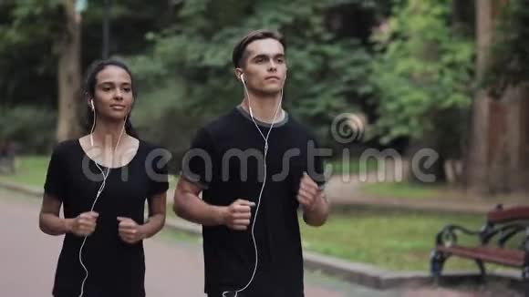 英俊的年轻人和漂亮的Mousline女孩在耳机里看着轻松的微笑在公园的侧视视频的预览图