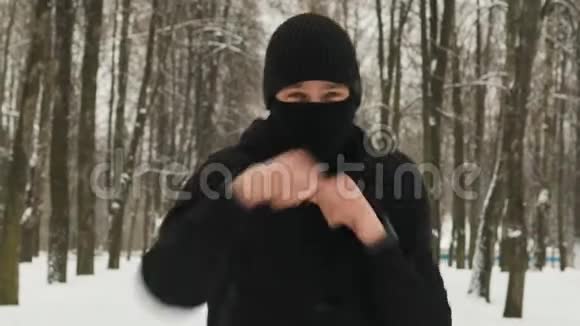 穿着黑色运动服的年轻人戴着头巾在冬天白雪皑皑的城市里表演拳打脚踢视频的预览图