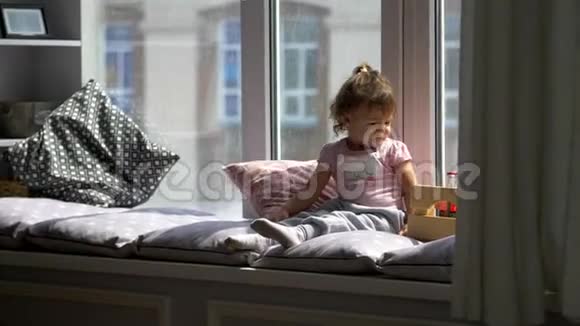 坐在窗台上可爱快乐的小女孩的肖像视频的预览图