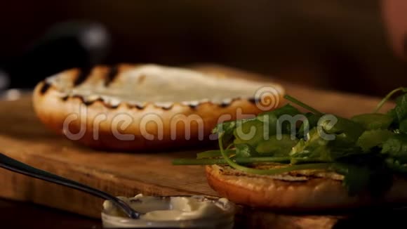 工艺汉堡正在黑暗的房间背景下烹饪库存录像把白色酸奶油酱贴在烤面包上视频的预览图