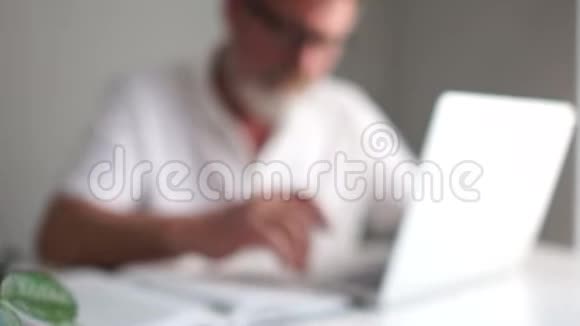 一位留着胡子戴着眼镜拿着笔记本电脑工作的白发成熟男人的肖像公司职员视频的预览图