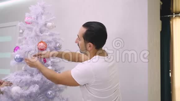 在皮贾马的男人用五颜六色的玻璃包装饰圣诞树视频的预览图