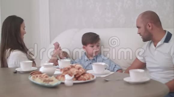 当爸爸和坐在茶几旁的儿子说话时年轻的妈妈正在和她的小男孩玩耍视频的预览图
