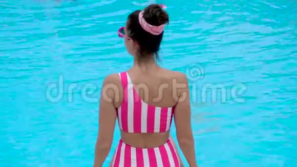 穿着条纹粉色泳衣的年轻女孩坐在泳池边视频的预览图