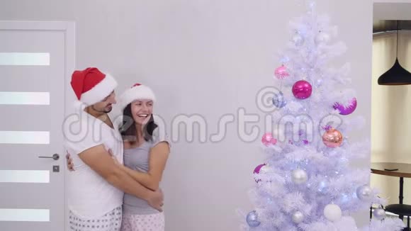 可爱的夫妇看着美丽的圣诞树女人调整粉红色的玻璃球视频的预览图