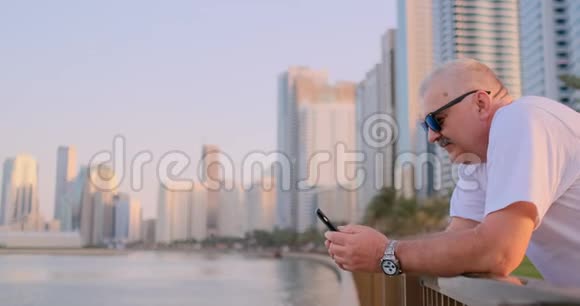 夏天一位站在海滨的老人在你的智能手机上写短信视频的预览图
