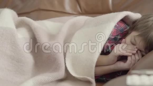 肖像小病童躺在沙发上盖着毯子在家打喷嚏桌子上放着不同的药片视频的预览图