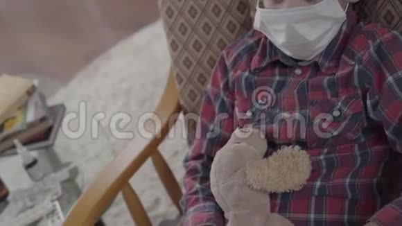特写肖像小病童坐在扶手椅上脸上戴着医疗面具手里拿着玩具视频的预览图